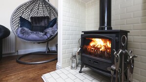 A cozy room with a black wood-burning stove, a hanging chair with cushions, and a white tiled wall. - JOIVY Greenknowes Lodge With Hot Tub And Wood Burning Stove (Kelty)