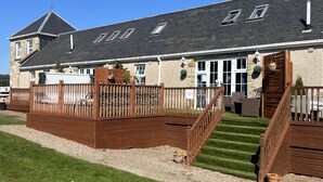A two-story building with a stone facade, a wooden deck, and a staircase leading to the upper level. - JOIVY Greenknowes Lodge With Hot Tub And Wood Burning Stove (Kelty)