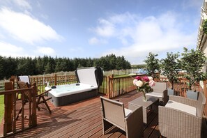 Une terrasse en bois avec un jacuzzi, des meubles en osier et une vue sur un lac.