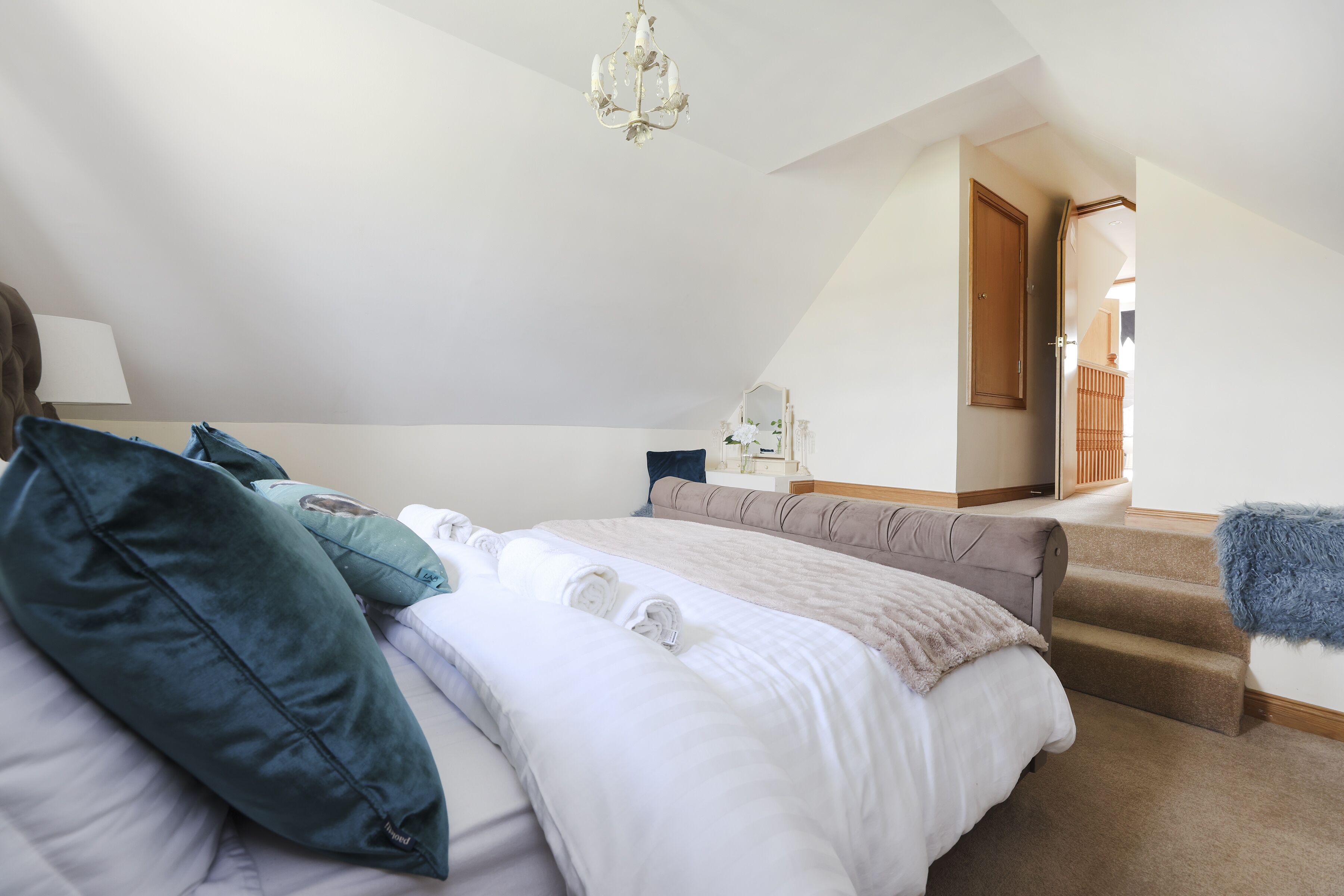 A bedroom with a large bed, a nightstand, a dresser, and a staircase leading to an upper level.