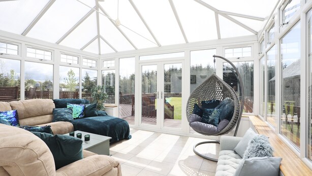 A conservatory with a glass ceiling, a hanging chair, and a cushioned sofa. - JOIVY Greenknowes Estate With Hot Tub And Bar (Kelty)