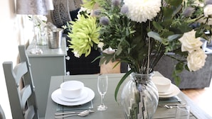 A dining table set with white plates, silverware, and a clear vase with flowers. - JOIVY Greenknowes Estate With Hot Tub And Bar (Kelty)