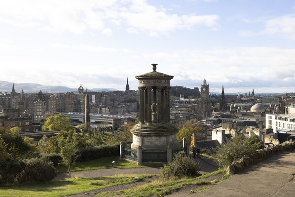 A cityscape with a prominent historical monument in the foreground, surrounded by lush greenery and a clear sky. - JOIVY Observatory House (Edinburgh)
