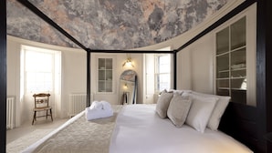 Ein Schlafzimmer mit einem großen Bett, einem Holzstuhl, einem Heizkörper und einem Fenster.