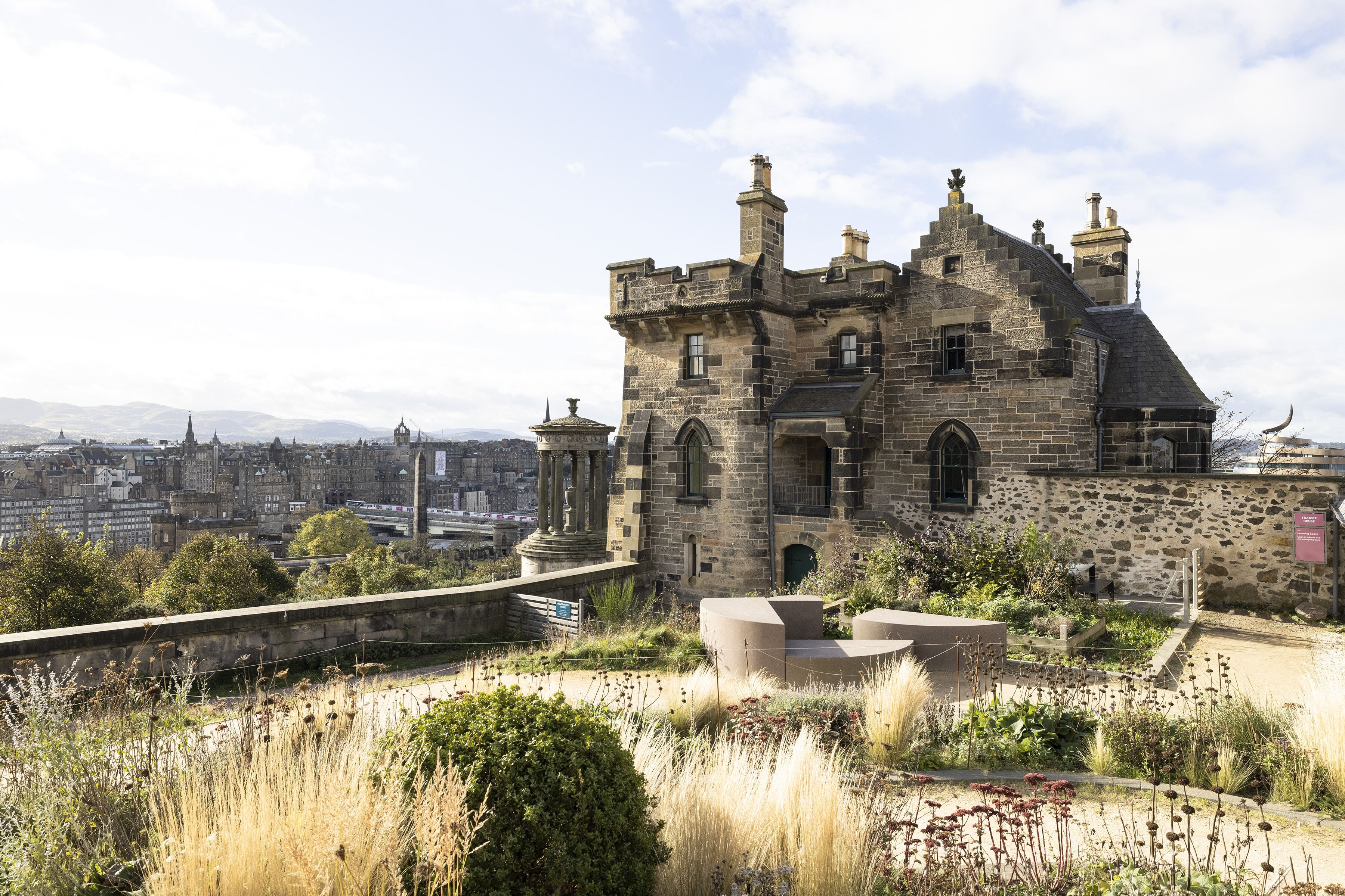 A historic stone building with a turreted roof, surrounded by a landscaped garden with pathways and benches.