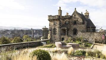 A historic stone building with a turreted roof, surrounded by a landscaped garden with pathways and benches.