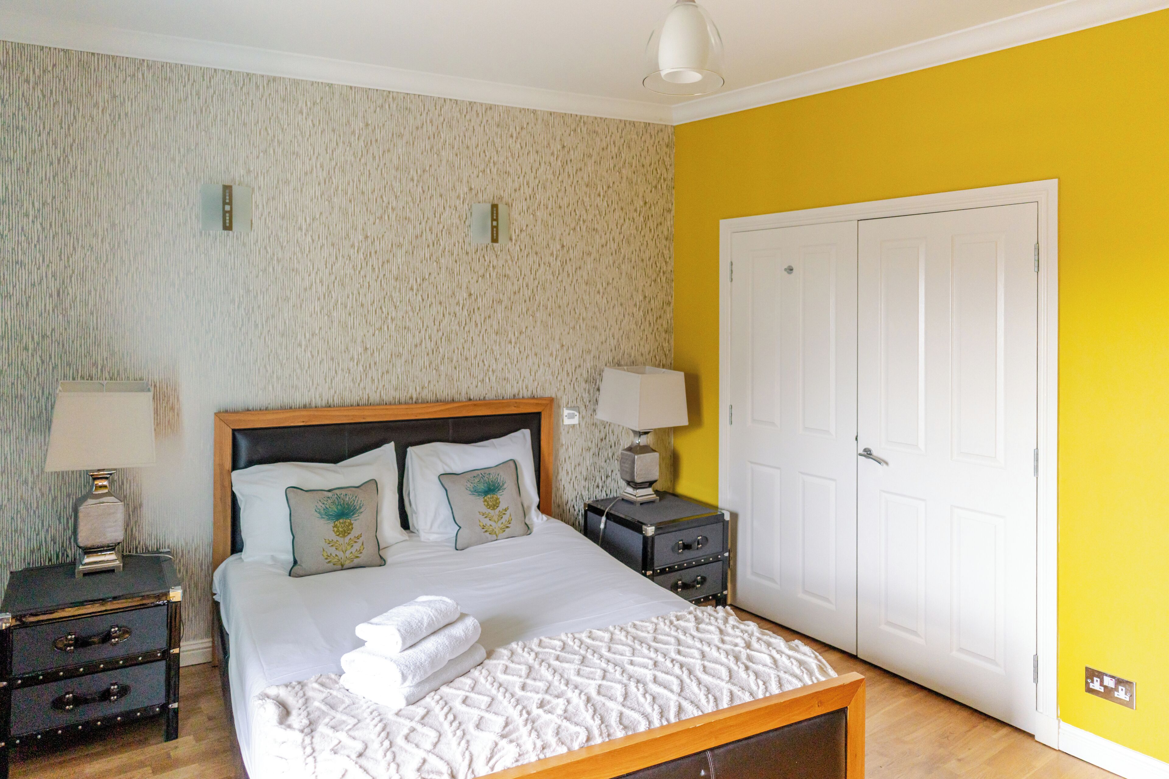 A bedroom with a wooden bed, two bedside tables, a white door, and a textured wallpaper wall.