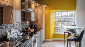Een moderne keuken met roestvrijstalen apparatuur, een eettafel met glazen blad en uitzicht op de stad door een groot raam.
