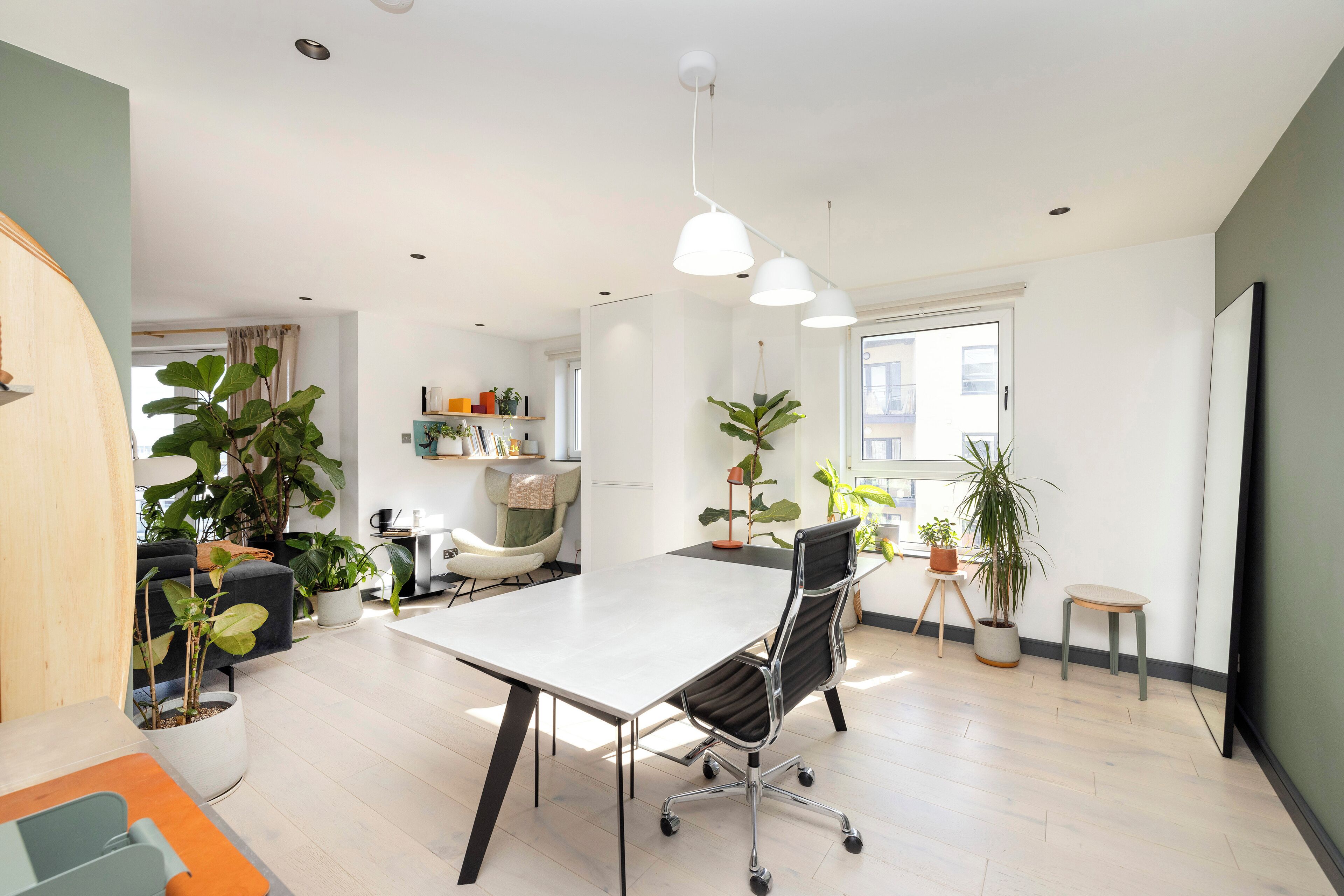 A modern, well-lit room with a large table, a comfortable chair, and several potted plants.