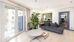 Ett modernt vardagsrum med en grå soffa, ett runt soffbord och en stor krukväxt.