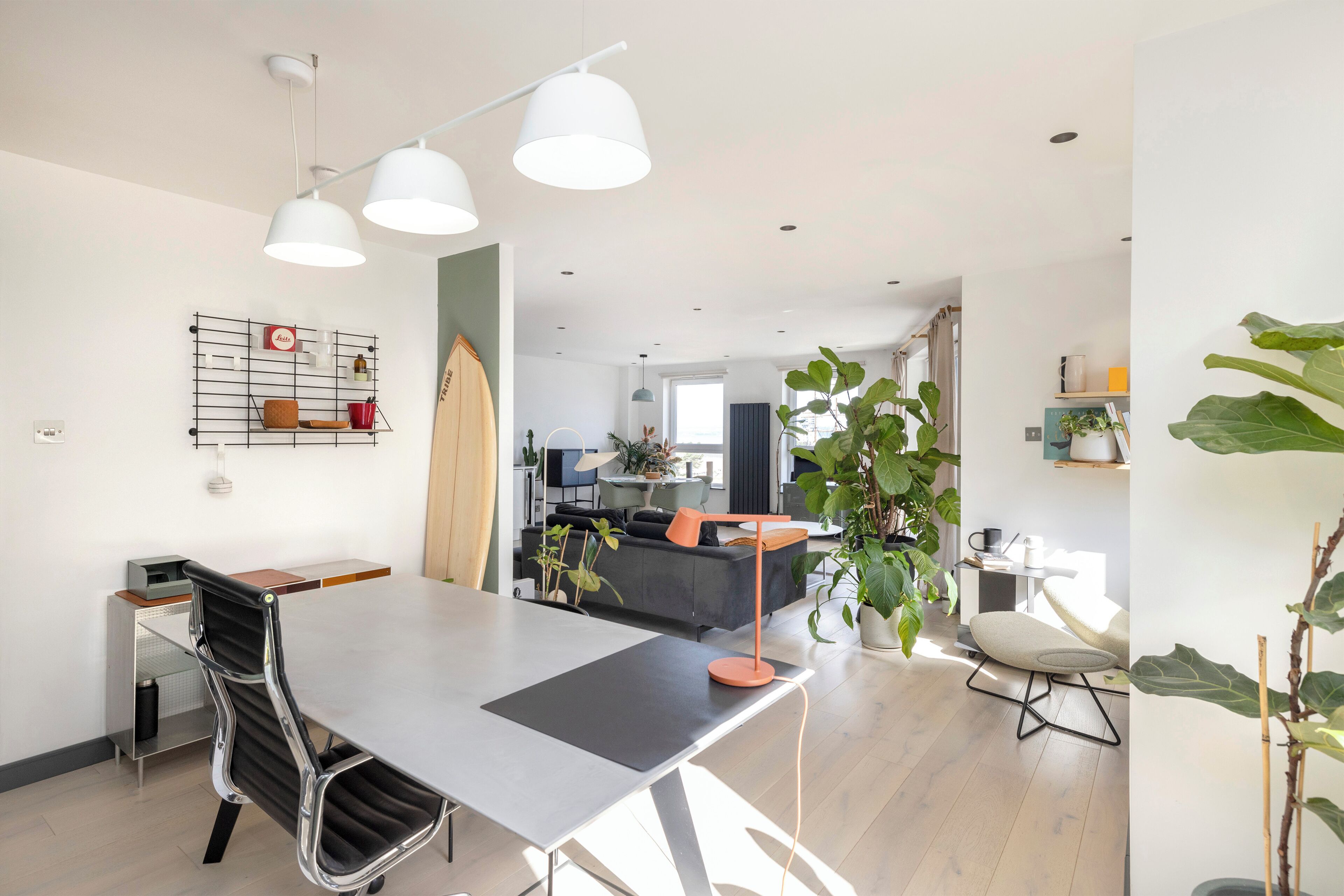 Ein moderner Essbereich mit Tisch, Stühlen und Pendelleuchten. Im Hintergrund ist eine Küchenzeile mit Sofa und Esstisch zu sehen.