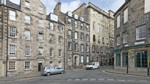 A street view with historic stone buildings, a car parked on the side, and a shop with a sign reading "Candlemaker." - JOIVY Spacious 3 Bed Apartment In The Old Town (Edinburgh)