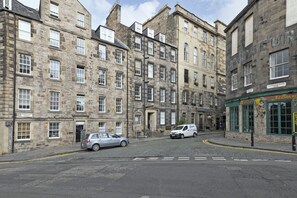 A street view with historic stone buildings, a car parked on the side, and a shop with a sign reading "Candlemaker." - JOIVY Spacious 3 Bed Apartment In The Old Town (Edinburgh)