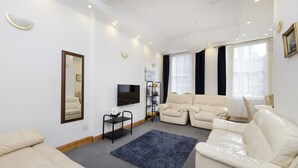 A modern living room with a beige sofa, a blue rug, and a flat-screen TV. - JOIVY Spacious 3 Bed Apartment In The Old Town (Edinburgh)