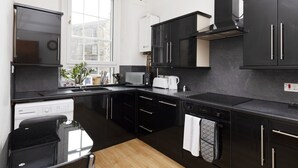 A modern kitchen with black cabinets, a microwave, a toaster, and a dishwasher. - JOIVY Spacious 3 Bed Apartment In The Old Town (Edinburgh)
