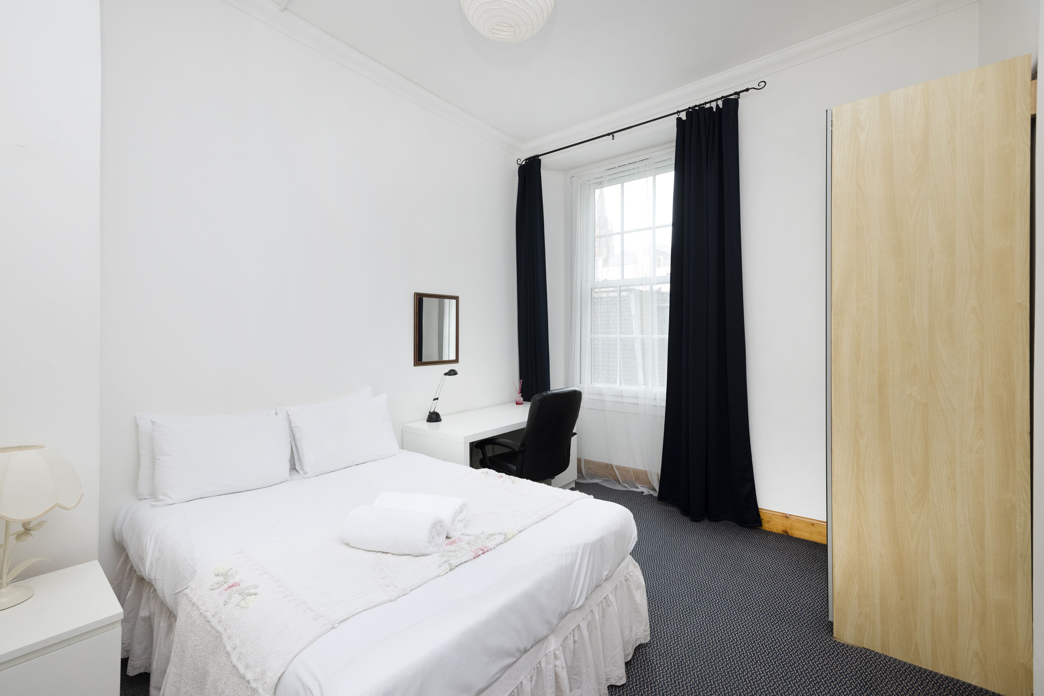 A hotel room with a bed, a desk, a chair, a mirror, and a wardrobe.