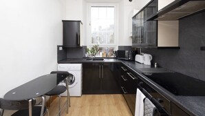 A compact kitchen with a washing machine, a sink, a microwave, and a stove. - JOIVY Spacious 3 Bed Apartment In The Old Town (Edinburgh)