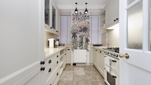 Une cuisine avec des meubles blancs, un sol carrelé, une cuisinière et un rideau décoratif à motifs floraux.