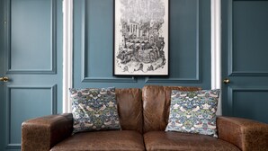 Un canapé en cuir marron agrémenté de coussins à motifs floraux, placé devant un mur de couleur turquoise, avec une œuvre d'art en noir et blanc encadrée au-dessus.