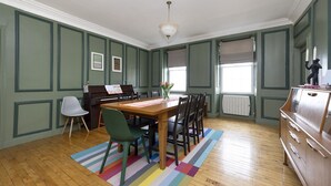 Un coin repas avec un piano, une table entourée de chaises, un tapis coloré et une commode.