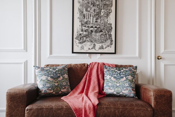 A brown leather sofa with floral-patterned cushions and a red throw blanket.