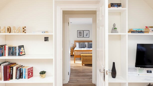 A hallway with white shelves on either side, leading to a bedroom with a wooden bed and a TV on the right. - JOIVY Inviting Flat Near Edinburgh Castle W/ Parking (Edinburgh)