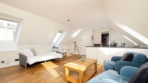 A spacious loft apartment with a high ceiling, wooden flooring, a dining area, a kitchenette, and a large window providing natural light. - JOIVY Inviting Flat Near Edinburgh Castle W/ Parking (Edinburgh)