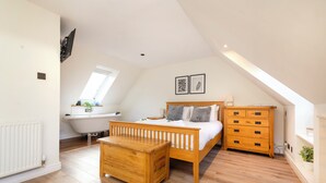 A bedroom with a sloped ceiling, a wooden bed, a wooden dresser, a wooden nightstand, a white radiator, and a skylight. - JOIVY Inviting Flat Near Edinburgh Castle W/ Parking (Edinburgh)