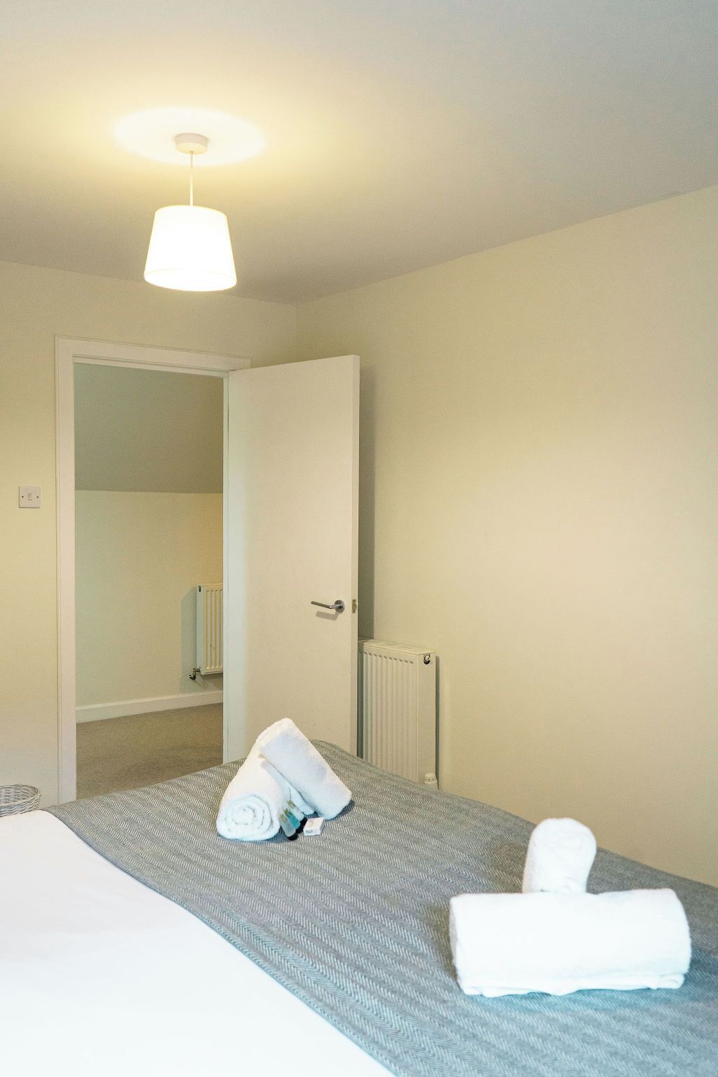 Ett hotellrum med en säng, ett element, en dörr och en taklampa.