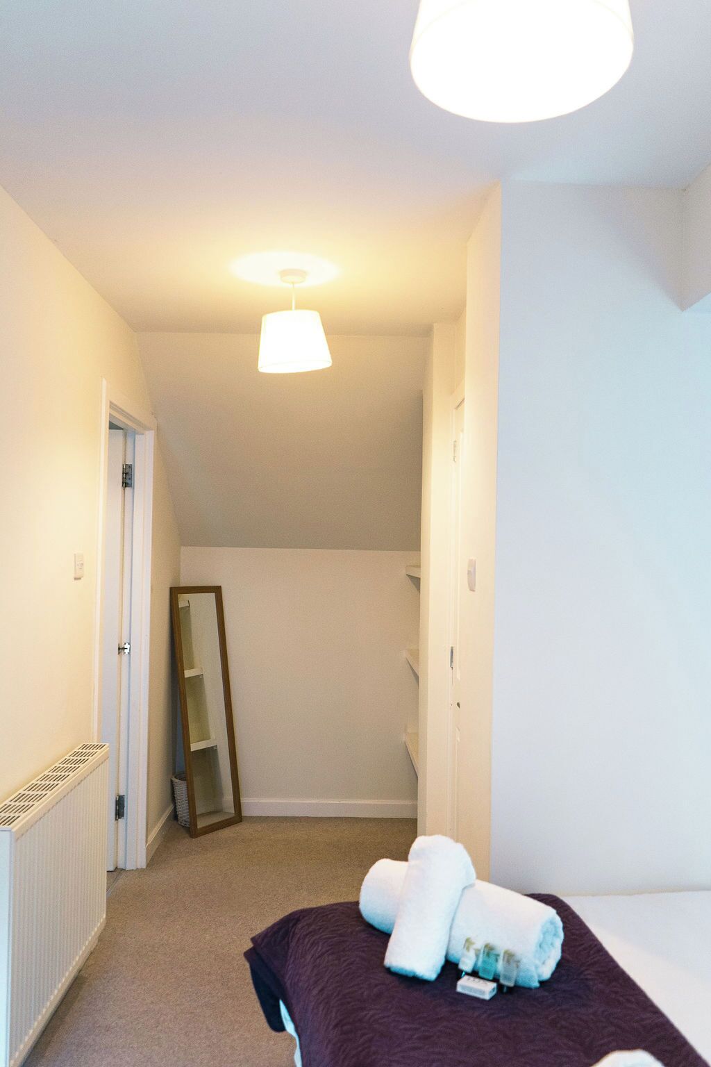 A hotel room with a bed, a large mirror, a radiator, and a ceiling light.
