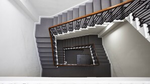 A modern staircase with a wooden handrail and black metal railings, leading to a landing with a small enclosed area. - JOIVY Splendid 2-Br Apartment In New Town (Edinburgh)
