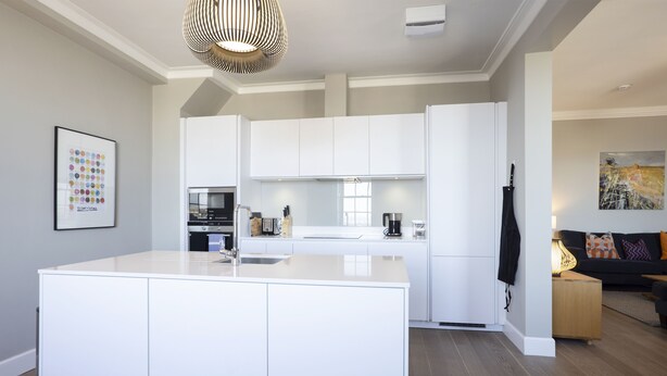 A modern kitchen with white cabinetry, a central island, and a dining area with a black sofa and colorful cushions. - JOIVY Splendid 2-Br Apartment In New Town (Edinburgh)
