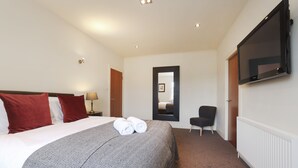 A hotel room with a large bed, a TV mounted on the wall, a chair, and a door leading to another room. - JOIVY Executive 2-Bed Apt With Stunning Roof Terraces (Edinburgh)