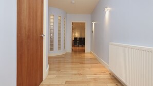 A hallway with wooden flooring, a white radiator, and a door leading to a room with a glass-fronted cabinet. - JOIVY Executive 2-Bed Apt With Stunning Roof Terraces (Edinburgh)
