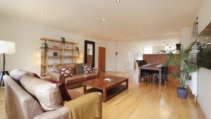 A spacious living room with a wooden coffee table, leather sofas, and a dining area with a table and chairs. - JOIVY Executive 2-Bed Apt With Stunning Roof Terraces (Edinburgh)