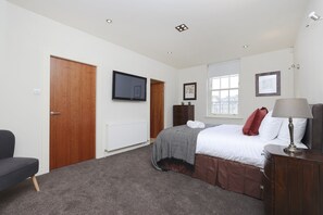 A bedroom with a bed, a TV mounted on the wall, a window, and a door.
