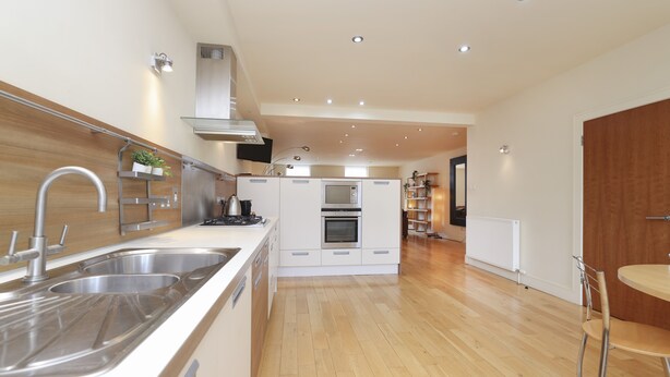 A modern kitchen with stainless steel appliances, wooden flooring, and a central island. - JOIVY Executive 2-Bed Apt With Stunning Roof Terraces (Edinburgh)