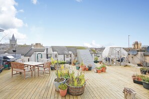 A rooftop terrace with a wooden table and chairs, surrounded by potted plants and a greenhouse structure. - JOIVY Modern 1-Br Apt W/ Communal Terrace In Trendy Stockbridge (Edinburgh)