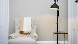 A corner room with a tufted armchair, a small round table, and a floor lamp. - JOIVY Modern 1-Br Apt W/ Communal Terrace In Trendy Stockbridge (Edinburgh)