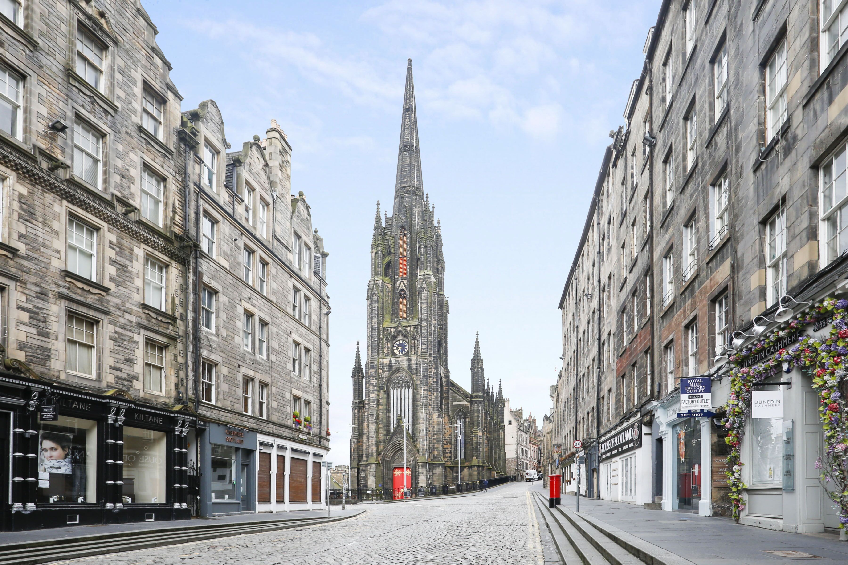 A cobblestone street with historic buildings on either side, leading to a prominent church with a tall spire.