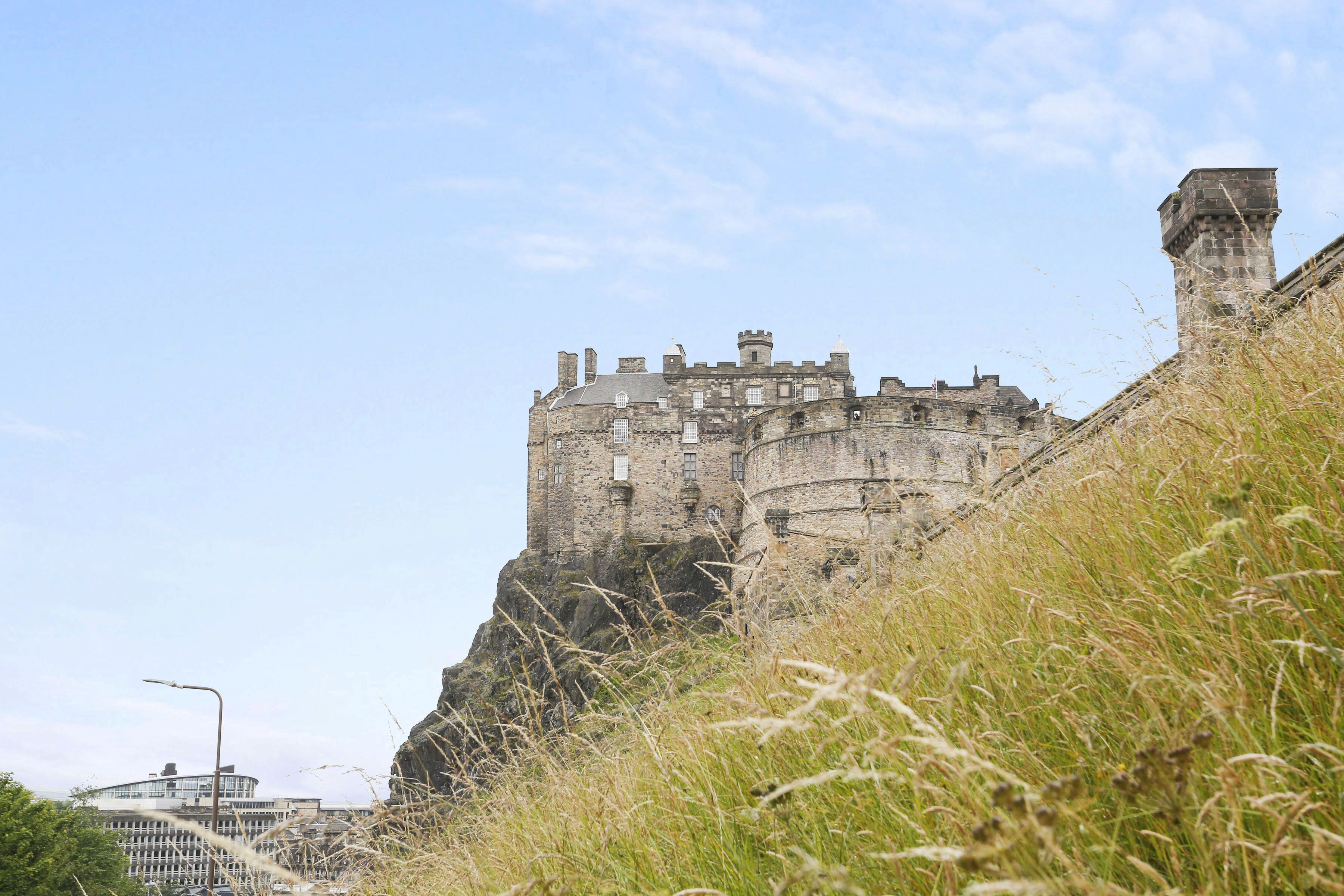 A historic stone castle perched on a cliff with a modern building in the background.