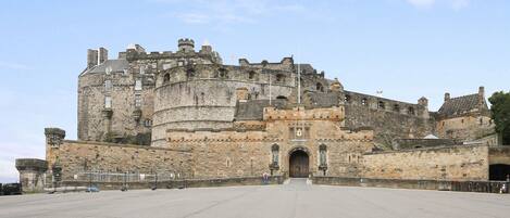 A historic stone castle with a large central tower, a fortified entrance, and a paved courtyard.