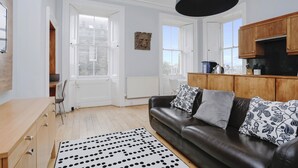A modern living room with a leather sofa, wooden cabinets, and a black and white patterned rug.