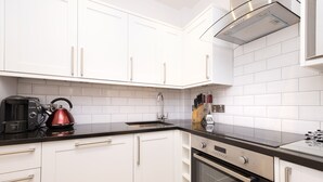 A modern kitchen with white cabinets, a black countertop, a coffee maker, and an oven. - JOIVY Charming 2-Bed Flat Near Edinburgh Castle (Edinburgh)