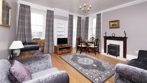 A living room with a fireplace, a television, and a dining area. - JOIVY Charming 2-Bed Flat Near Edinburgh Castle (Edinburgh)