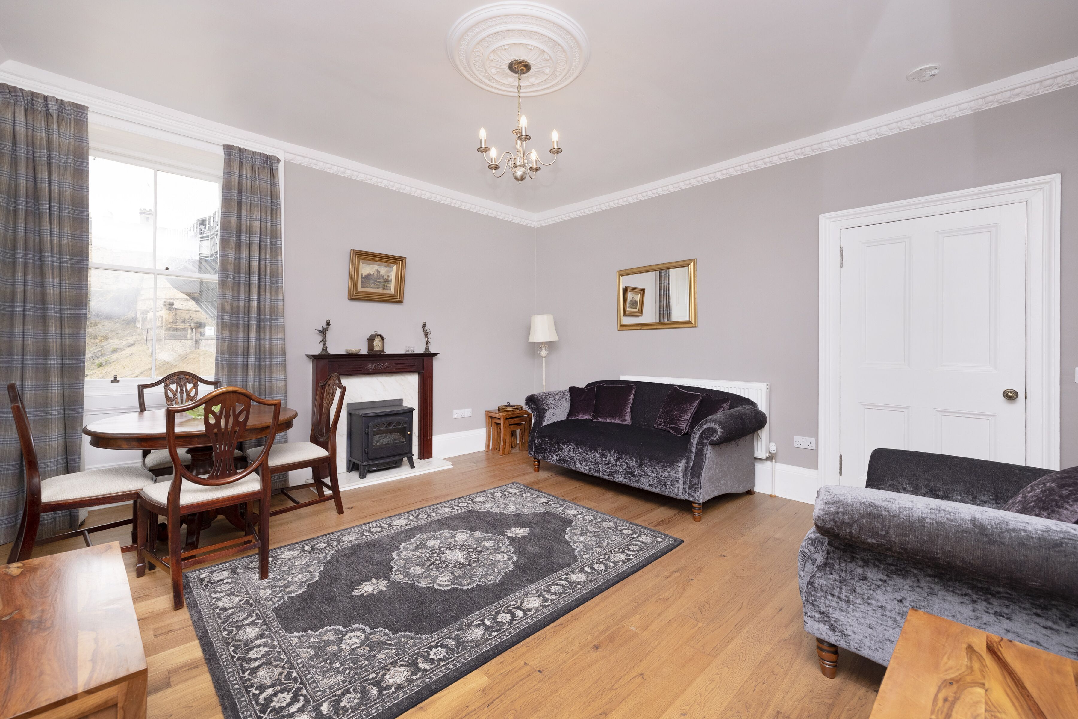 A living room with a fireplace, a sofa, a dining table with chairs, and a large rug.