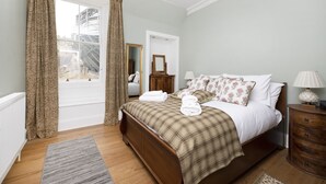 A bedroom with a bed, a nightstand, a mirror, and a window with curtains. - JOIVY Charming 2-Bed Flat Near Edinburgh Castle (Edinburgh)