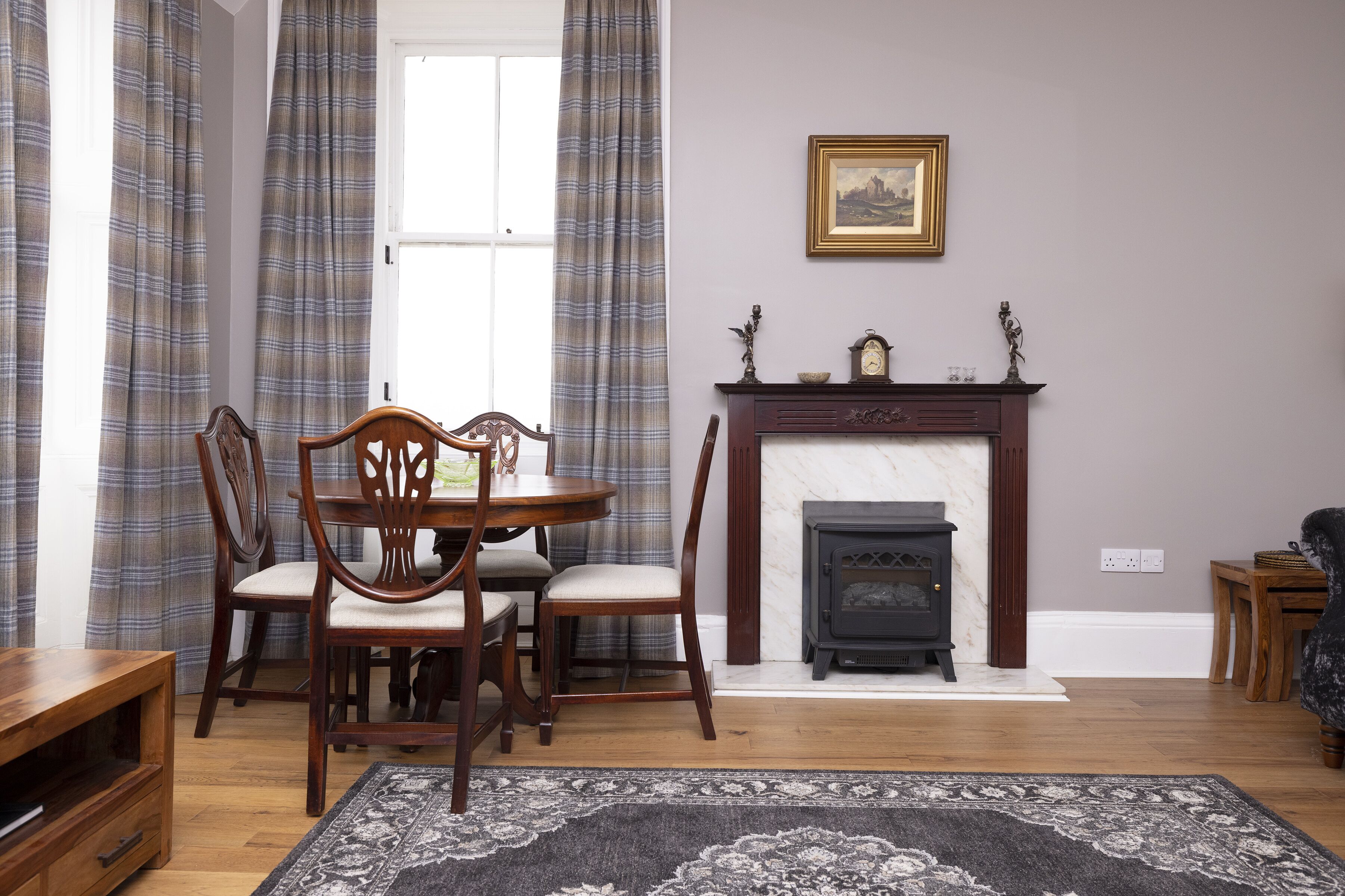 A dining area with a wooden table and chairs, a fireplace, and plaid curtains.