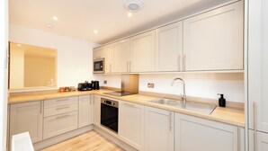 A modern kitchen with white cabinets, a stainless steel sink, and a built-in oven. - JOIVY 3BR Flat in Haymarket with Free Parking (Edinburgh)