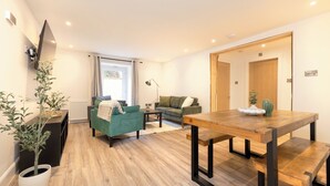A modern living room with a wooden dining table, two sofas, a potted plant, and a television mounted on the wall. - JOIVY 3BR Flat in Haymarket with Free Parking (Edinburgh)